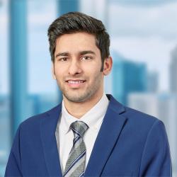 Man wearing blue blazer and grey tie smiles into the camera.