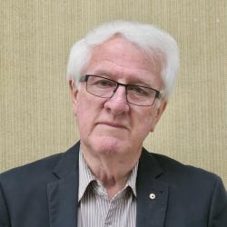 Chris, with white hair and glasses, looks at the camera