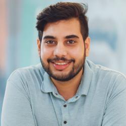 Bearded man wearing a light blue polo shirt smiles.