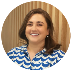 Carolina Sandler has shoulder-length brown hair. She is wearing a blue and white patterned shirt. She is smiling at the camera.