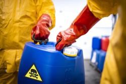 Two workers in hazmats holding a container of toxic chemicals
