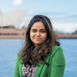 Woman wearing a green blazer smiles in front of the Sydney Opera House.