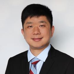 Man wearing suit and tie smiles into camera.