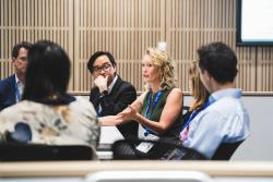 Lauren Solomon pictured in discussion with symposium attendees. Lauren is sitting in a table. 