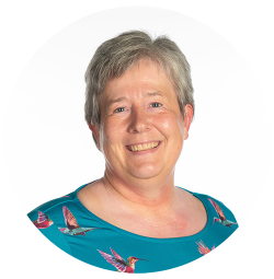 Professor Catherine Walshe has short grey hair. She is wearing a blue top with colourful birds on it.