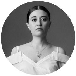 Young woman in black and white, looking at the camera with her dark hair tied back. She is wearing an off  the shoulder white top.