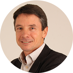 Man smiling and looking at the camera wearing a black suit with a business shirt