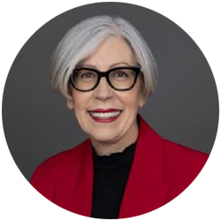 Women with short grey hair wearing black glasses, a black shirt and red jacket, smiling and looking at the camera