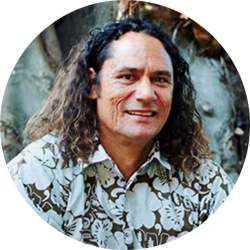 Man with shoulder length curly hair in a brown and white floral shirt, smiling and looking at the camera