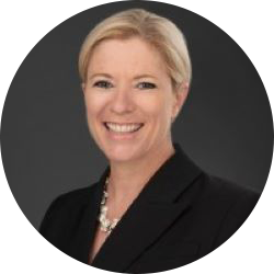 Woman with short blonde hair wearing a black suit jacket, smiling and looking at the camera