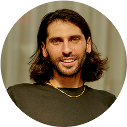 Man with shoulder length brown hair smiling and looking at the camera wearing a green tshirt