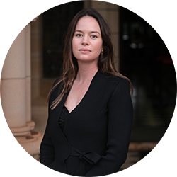Woman with long dark coloured hair wearing a black suit and black shirt smiling and looking at the camera