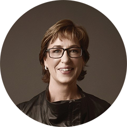 Woman with short brown hair and black glasses smiling and looking at the camera