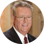 Man with short white hair and glasses wearing a suit and shirt smiling and looking at the camera