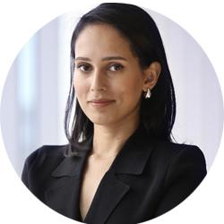 Woman with shoulder length black hair wearing a black suit jacket. Smiling and looking at the camera
