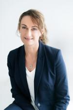 professional image of woman smiling at the camera - she is wearing a white shirt, blue blazer, her light brown hair is in a ponytail