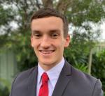 A headshot of Ethan who's dressed smartly in a grey suit and red tie, smiling to the camera.