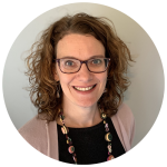 Dr Felicity Bright wears a black top, pink cardigan and a beaded necklace as well as glasses. She is smiling at the camera.