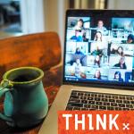 Laptop on desk showing a number of faces in a zoom meeting