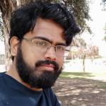 Profile photo of Madhav Vijayan. Madhav is standing in front of a tree in a park