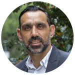 Adam Goodes smiling in an outdoor portrait shot in front of planted greenery.