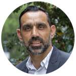 Adam Goodes smiling in an outdoor portrait shot in front of planted greenery. 