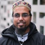 Chest up photo of Mofijur Rahman wearing a kufi looking at the camera