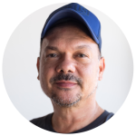 Dr Stephen Page AO smiling in an indoor portrait shot wearing a blue cap.