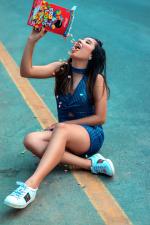 A young adult sitting on the ground pouring a box of colourful cereal into their mouth
