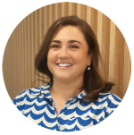 Carolina Sandler has shoulder-length brown hair. She is wearing a blue and white patterned shirt. She is smiling at the camera. 