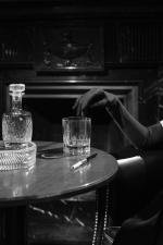 Black and white image, woman with black glove, decanter and glass on table