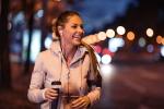 A woman dressed in pink jacket holding water bottle and smiling with headphones on