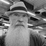 Black and white photo of Glenn Redmayne (a middle-aged man with a long white beard and a hat, facing the camera).