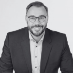 A man in a suit and glasses smiling